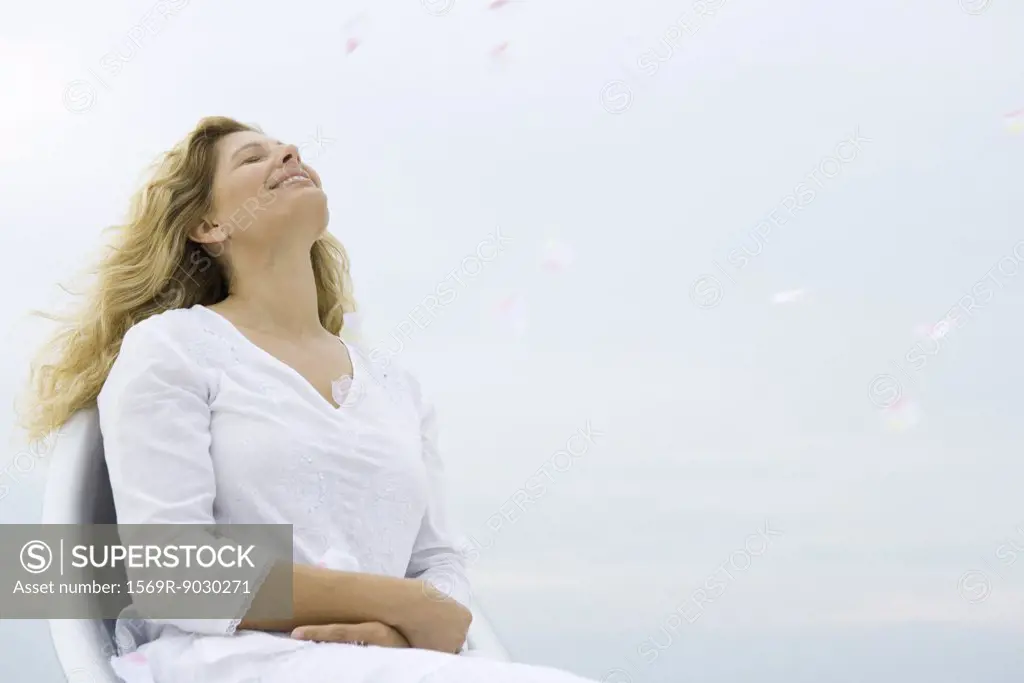 Woman sitting with eyes closed and head back, smiling, sky in background, low angle view