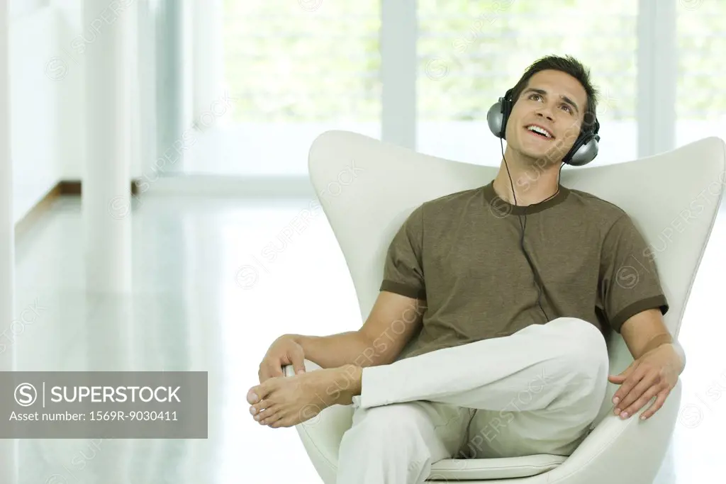 Young man sitting in chair listening to headphones, smiling