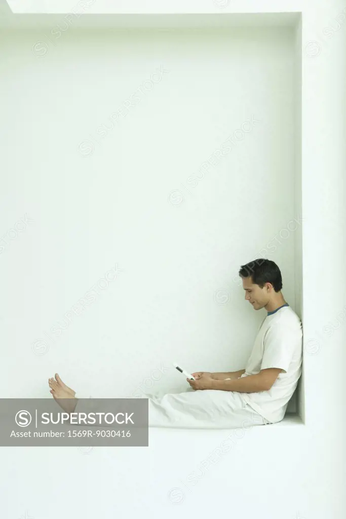 Man sitting on ledge using cell phone, full length, side view