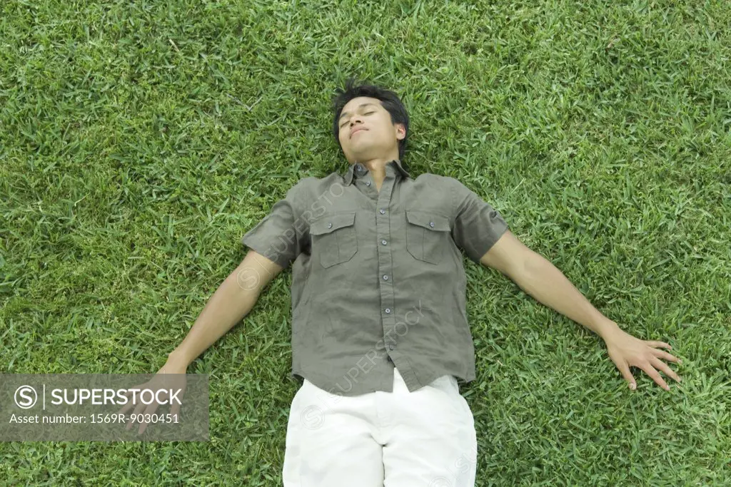 Man lying on back in grass, eyes closed