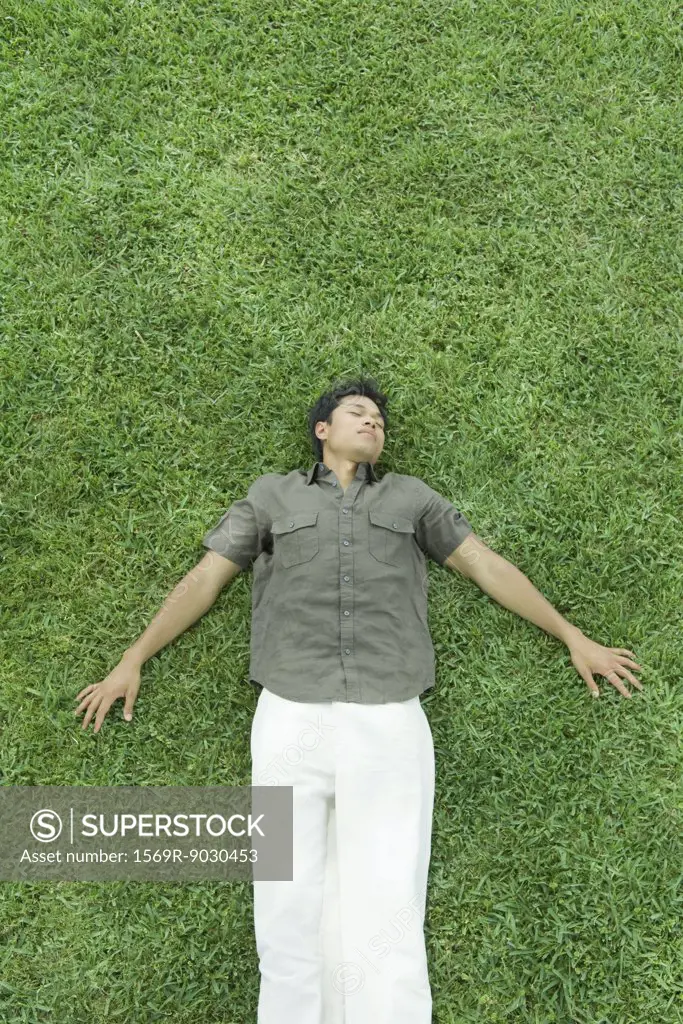 Man lying on back in grass, eyes closed, full length