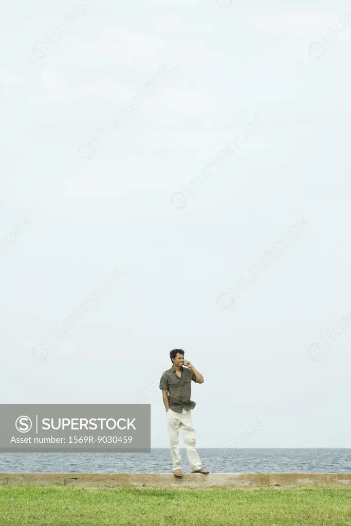 Man standing, using cell phone, body of water in background