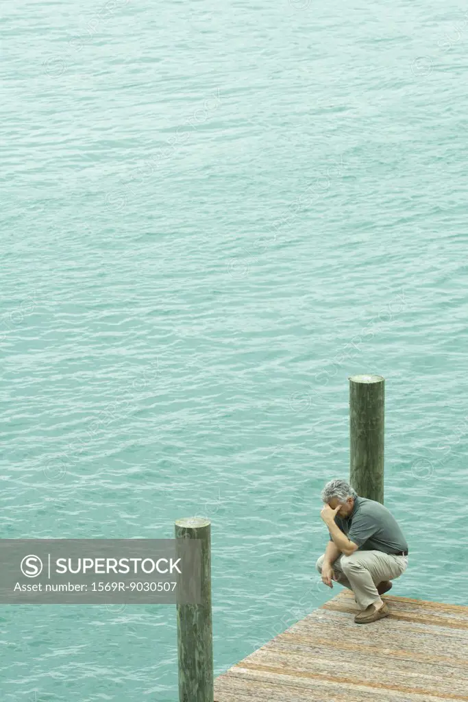 Man crouching on dock, holding head, high angle view