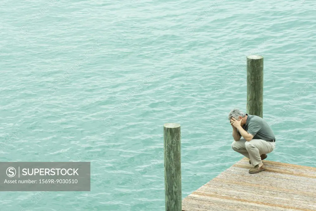 Man crouching on dock, holding head, high angle view