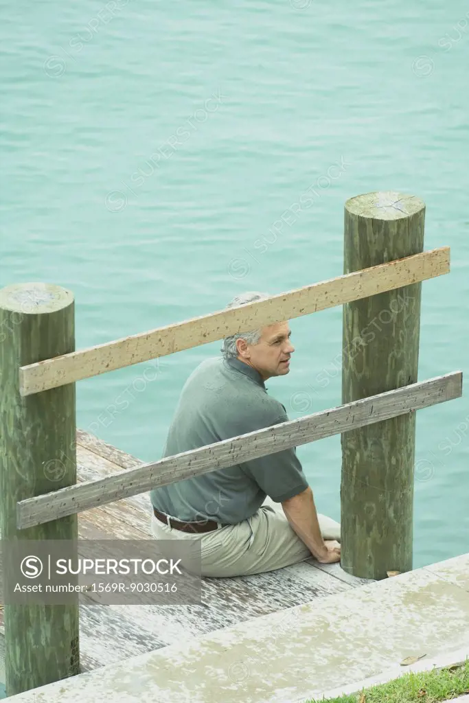 Man sitting on edge of dock, looking away, high angle view