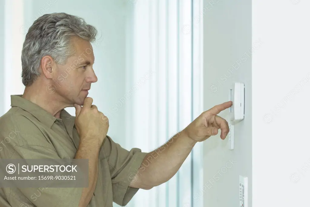 Mature man looking at control panel on wall, hand under chin, side view