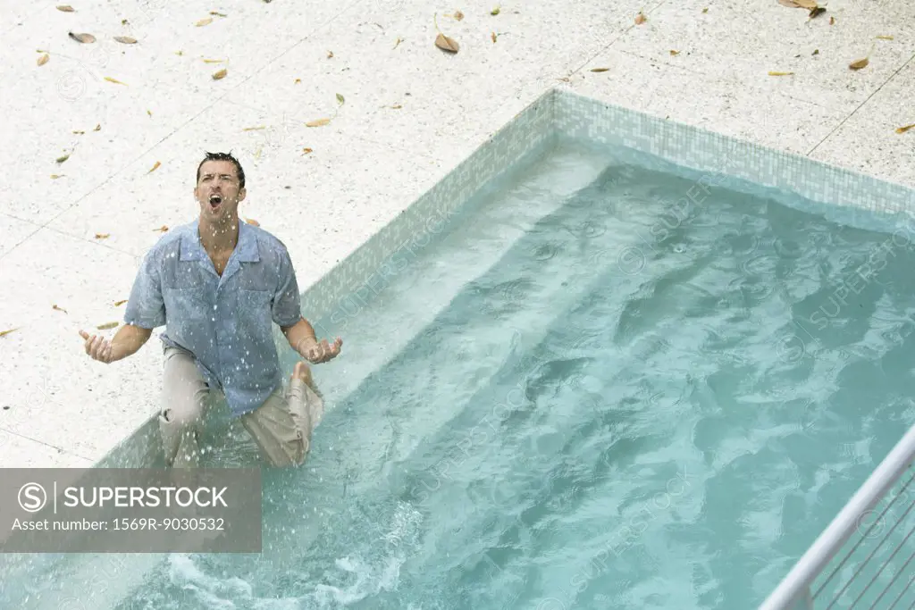 Man splashing in pool, fully clothed, shouting and gesticulating, high angle view