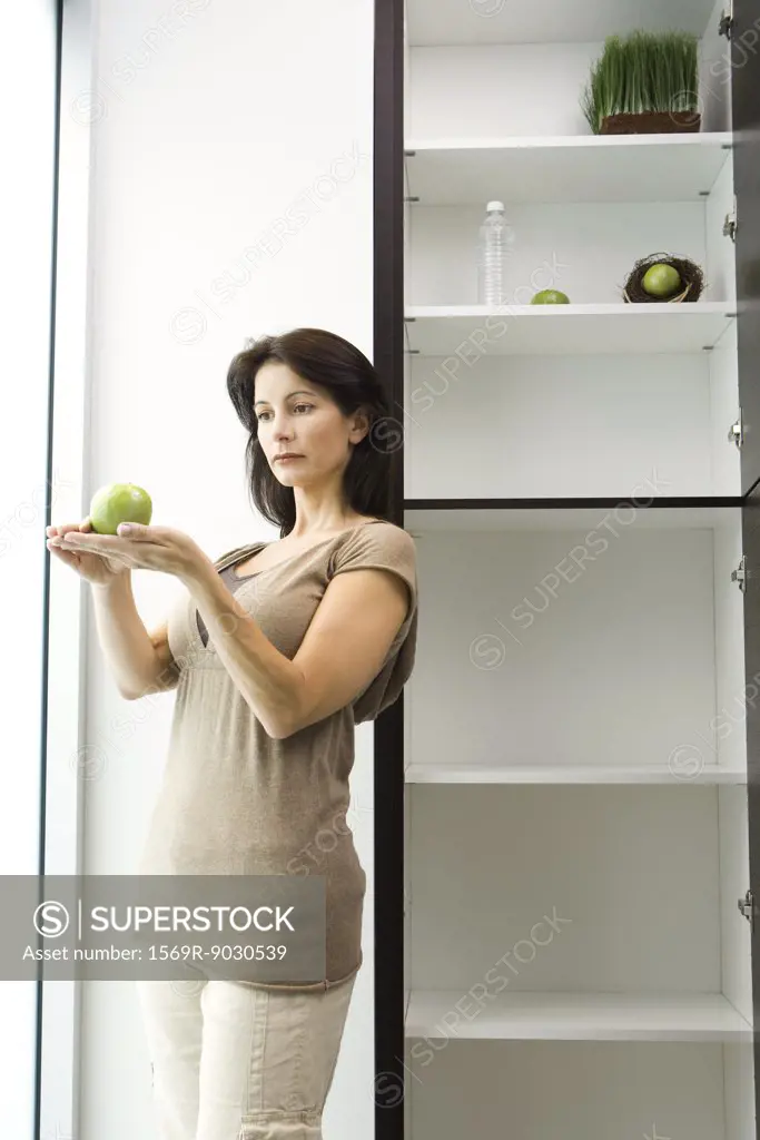 Woman standing by open pantry, apple on palms of hands