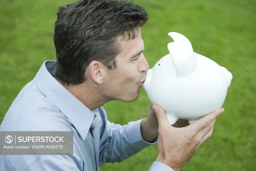 Man kissing piggy bank, side view