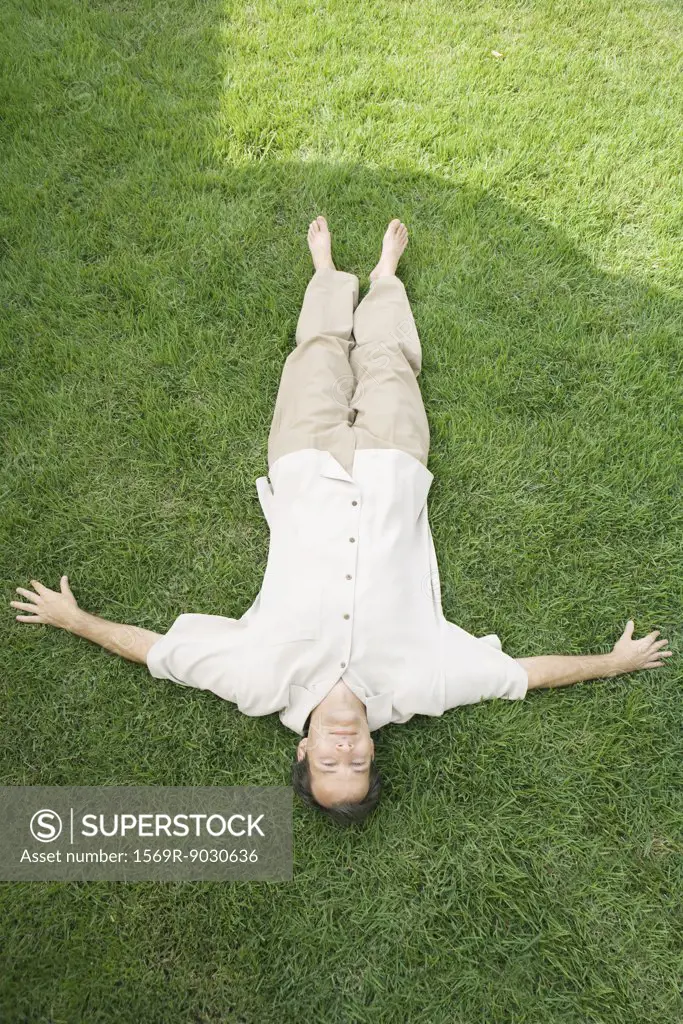 Man lying on back in grass, smiling at camera, high angle view