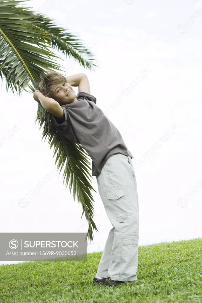 Boy leaning against palm branch, smiling at camera