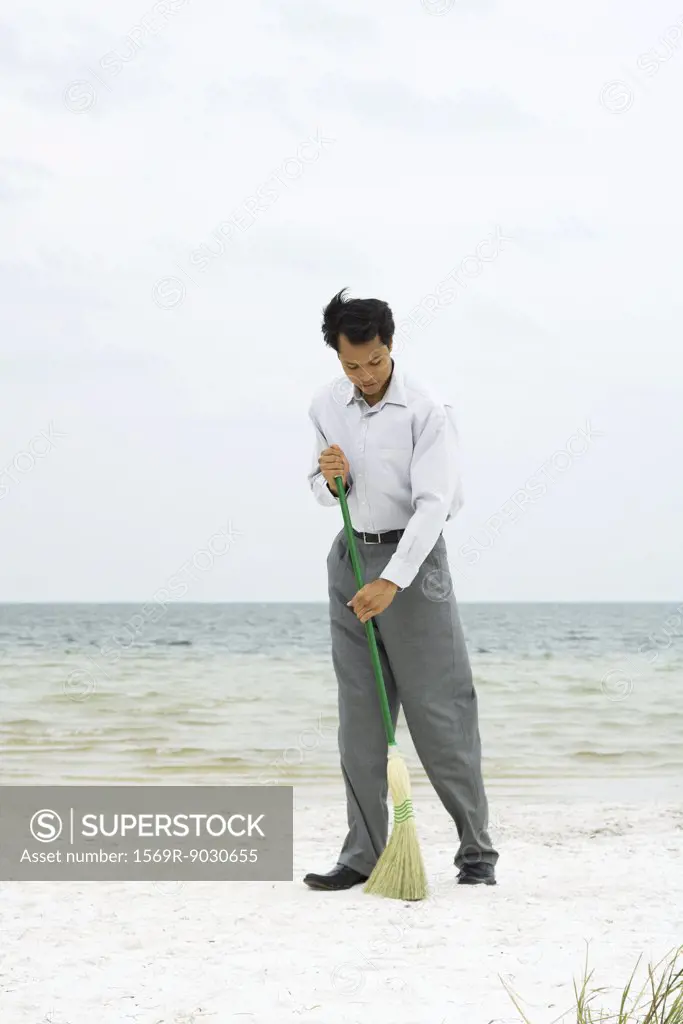 Man standing on beach sweeping with broom, full length