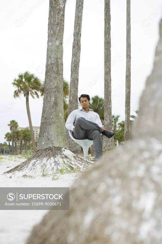 Man sitting in chair at the beach, looking at camera, low angle view