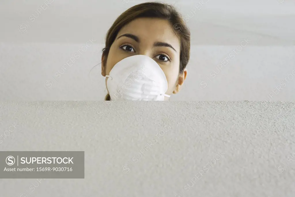 Woman wearing pollution mask, looking over ledge at camera