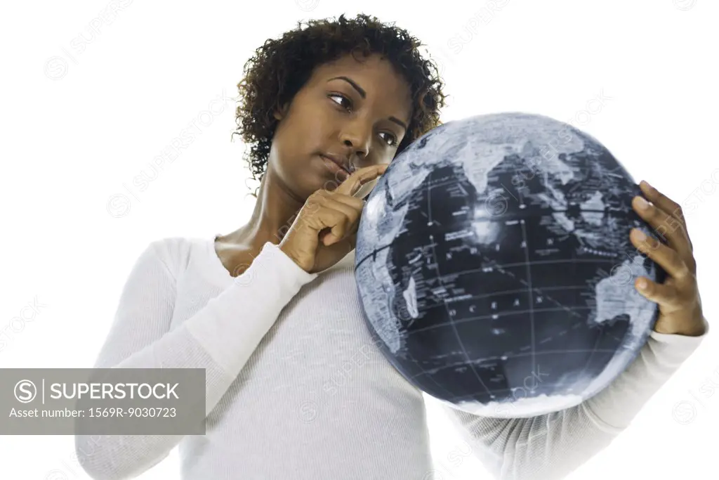Young woman looking at globe and pointing with finger