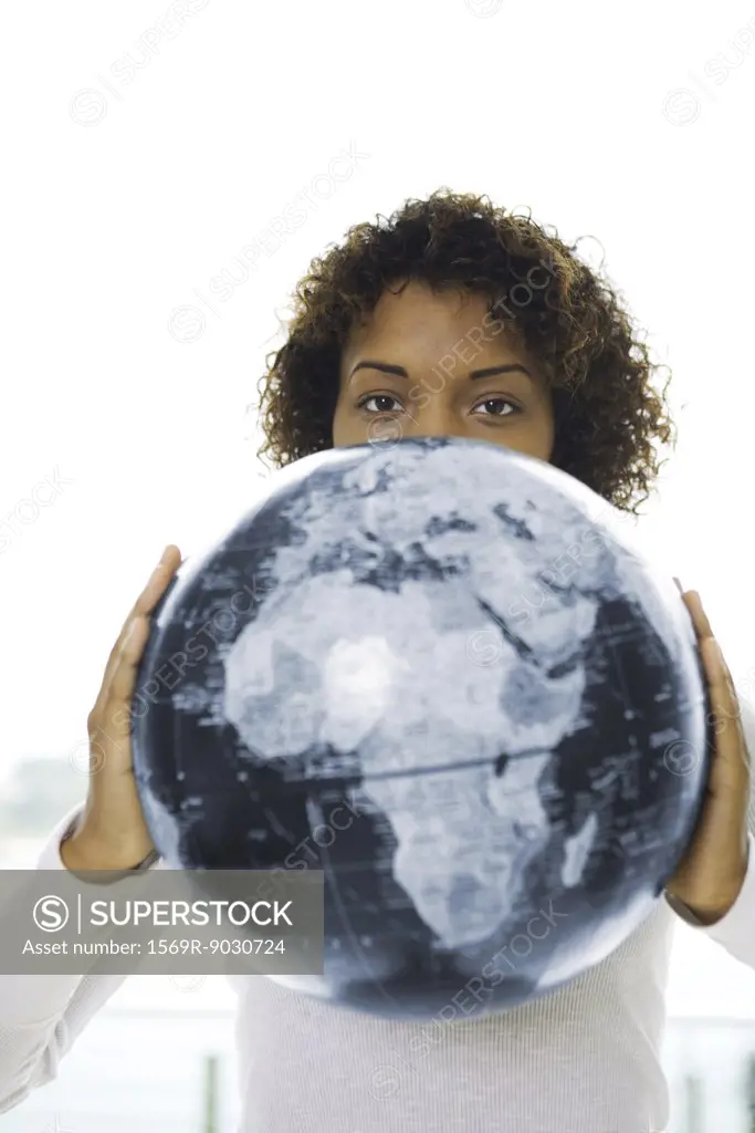 Young woman looking over globe at camera