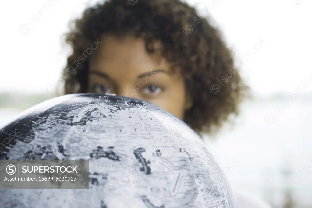 Woman looking over globe at camera, cropped view