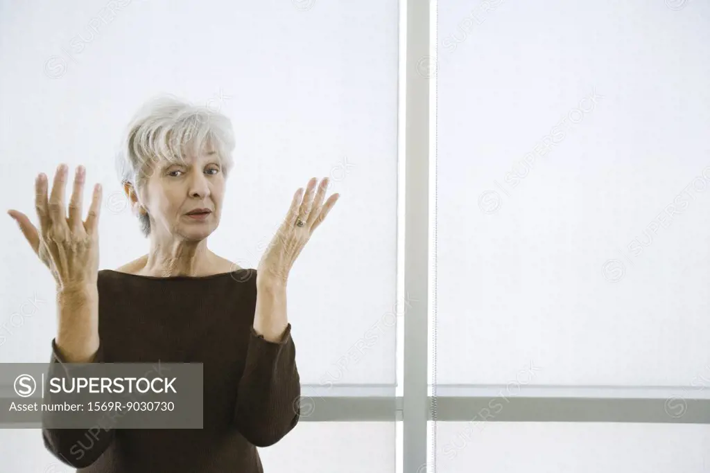 Senior woman with both hands raised, looking at camera