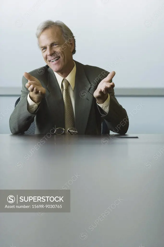 Businessman seated, gesturing with hands, smiling, looking away