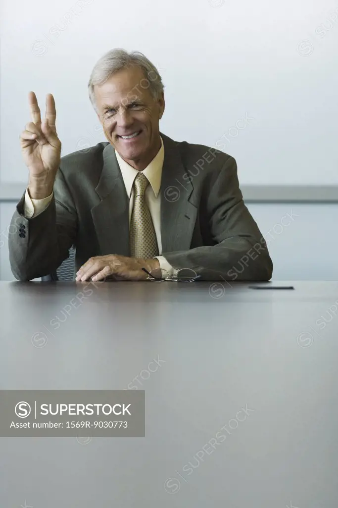 Businessman making peace sign, smiling at camera
