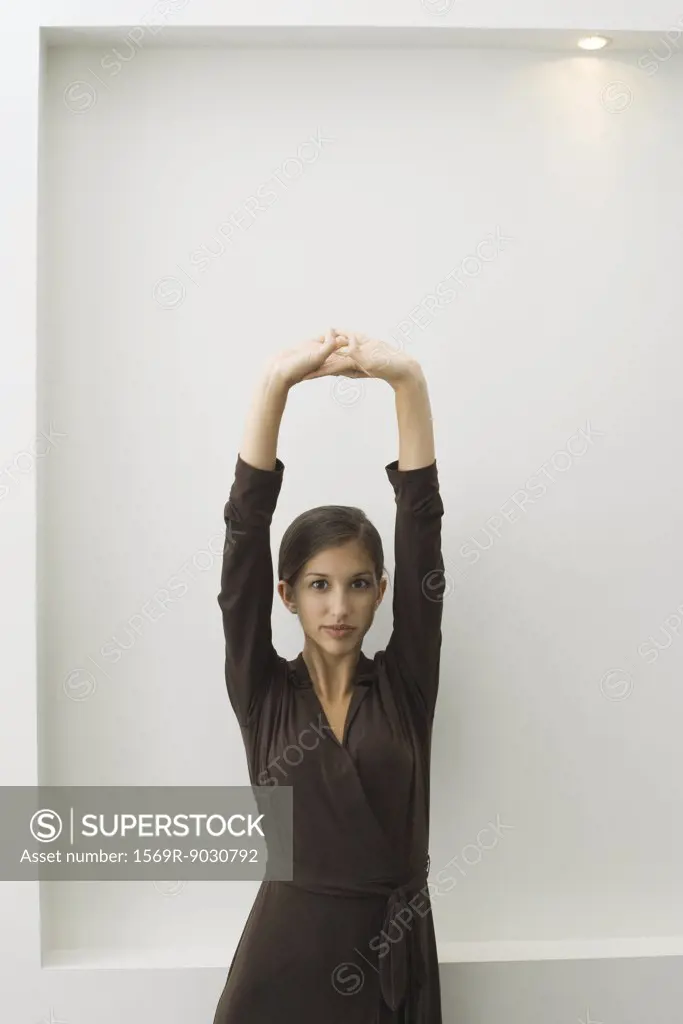 Teenage girl standing with arms raised, clasped hands, looking at camera