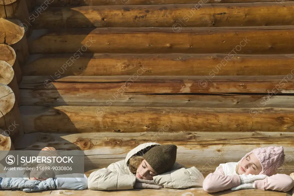 Three preteen or teen girls standing on deck of log cabin, resting heads on railing