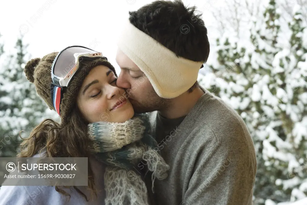 Young couple in winter clothing, man kissing woman on cheek