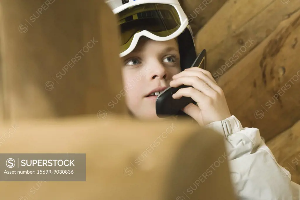Boy wearing ski goggles, using cell phone, cropped view