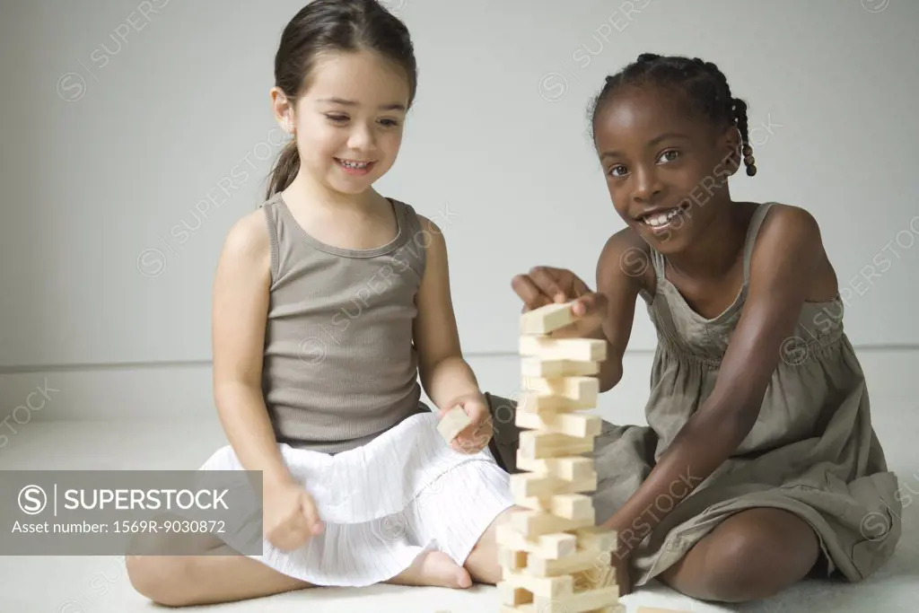 Two girls sitting on floor playing with blocks, one smiling at camera