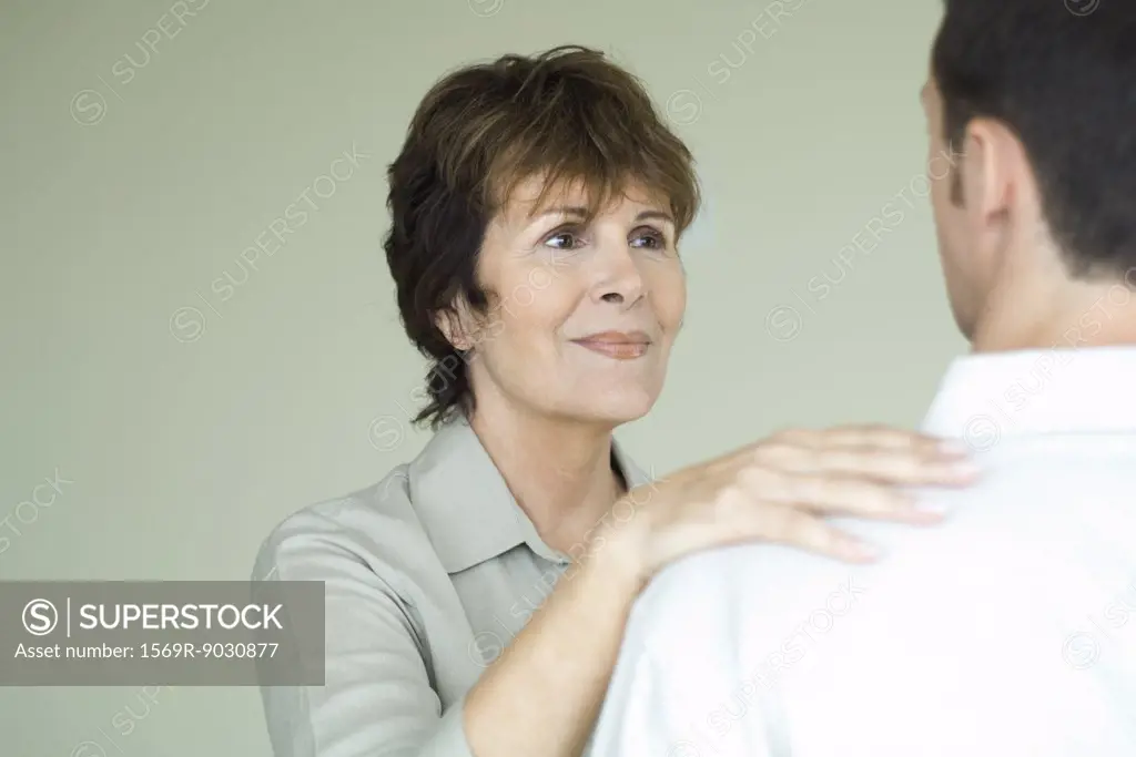 Senior woman standing in front of adult son with her hand on his shoulder, smiling