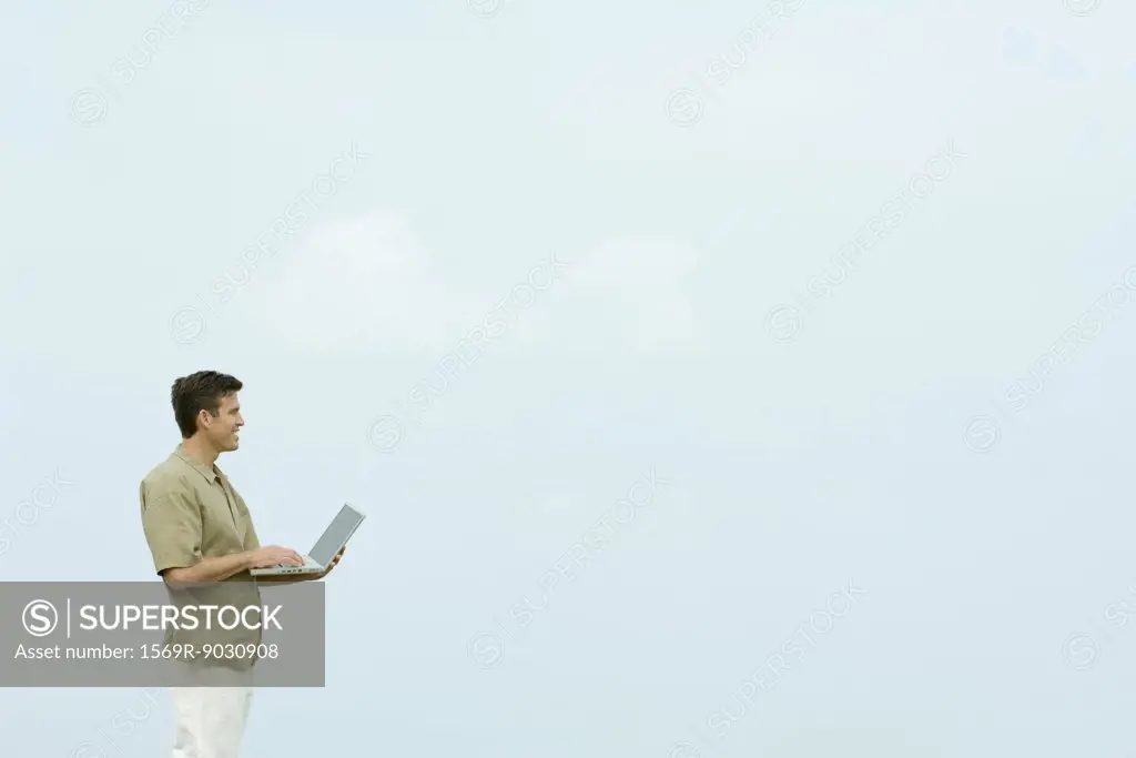 Man standing outdoors holding laptop computer, looking away