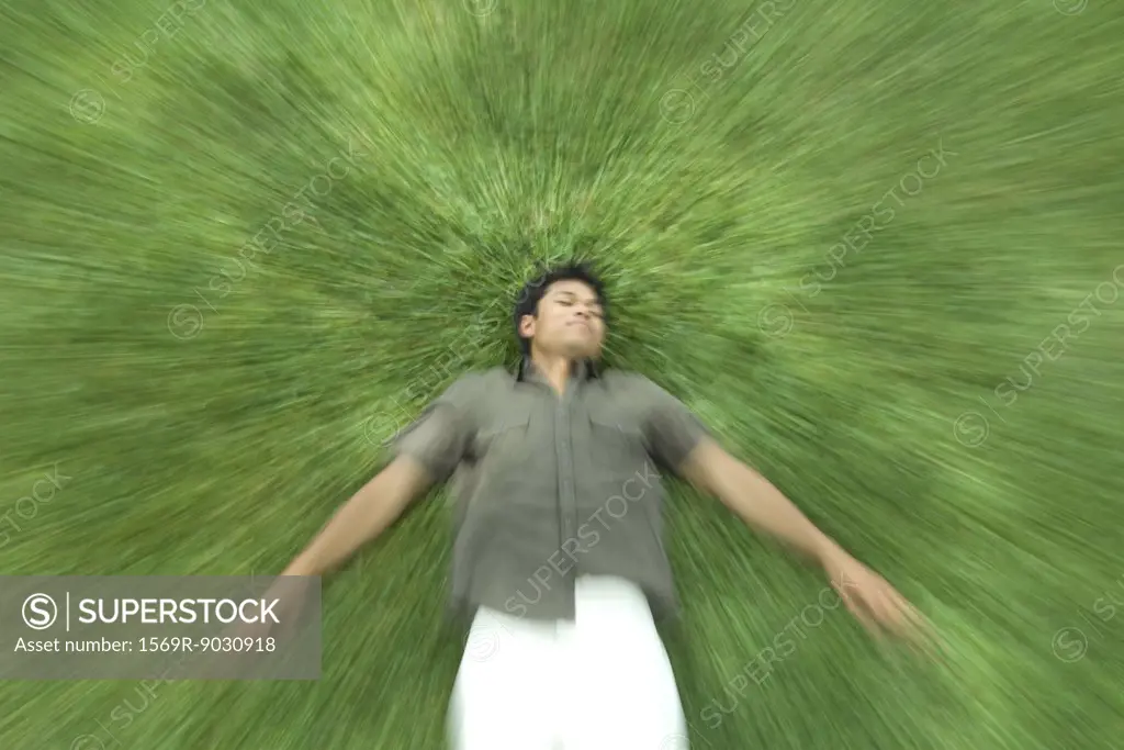 Man lying on back in grass with eyes closed, blurred motion