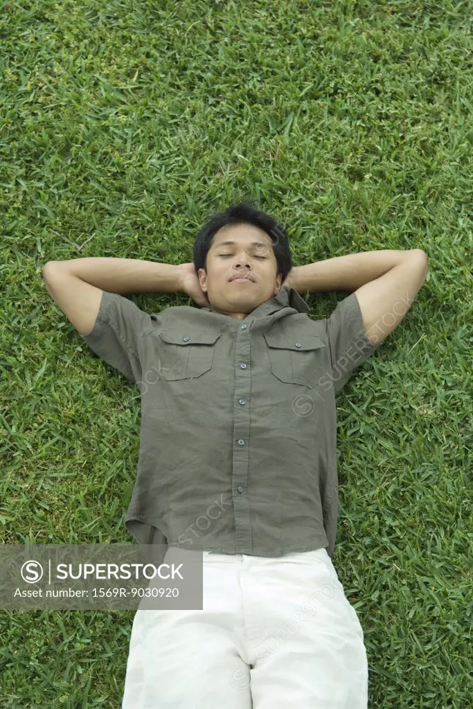 Man lying on back in grass with hands under head, eyes closed