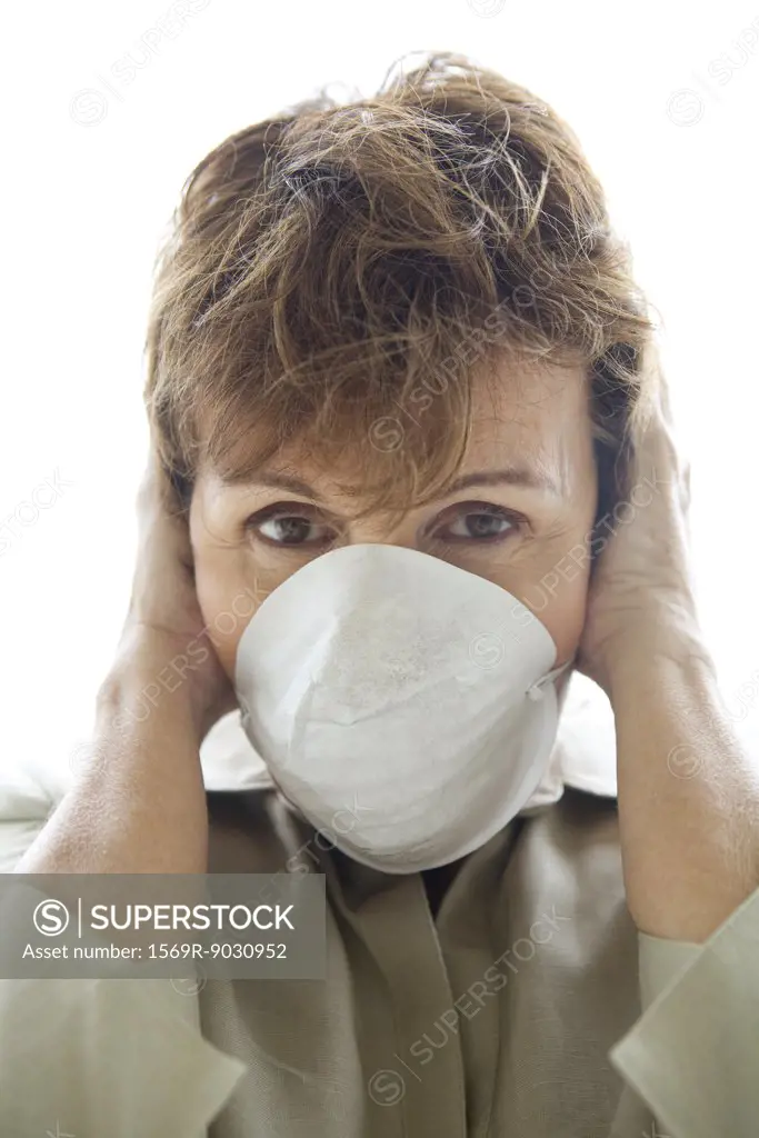 Woman with hands over ears wearing pollution mask, looking at camera