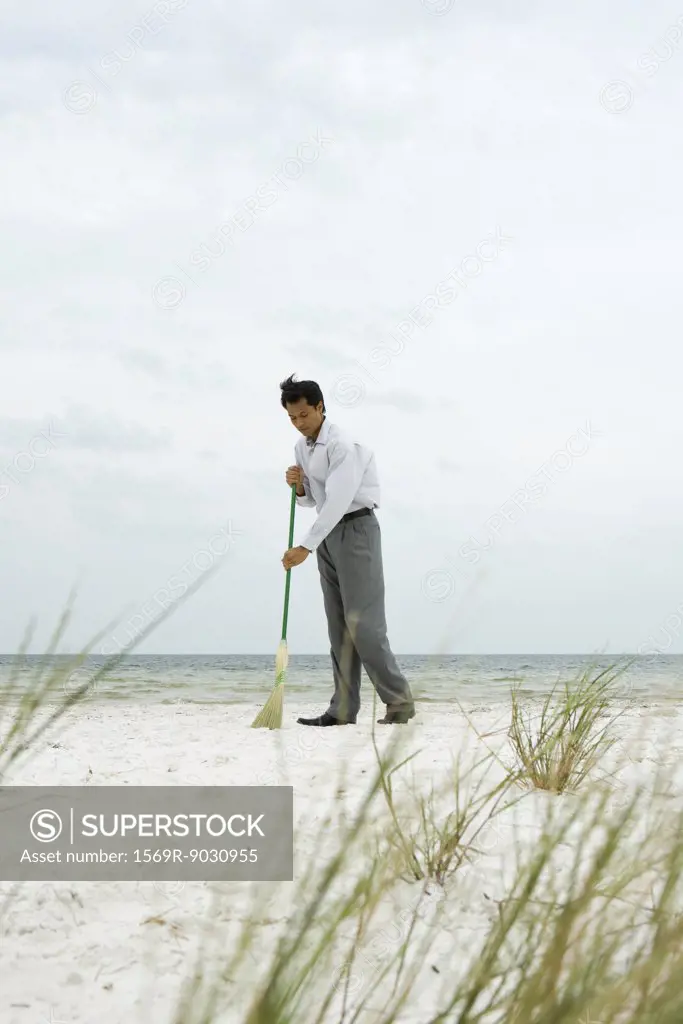 Man standing at the beach sweeping sand with broom