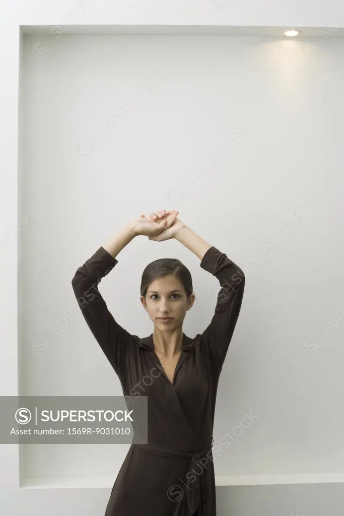 Young female leaning against wall with arms raised, looking at camera
