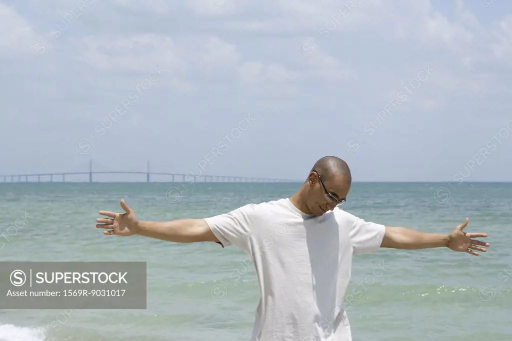 Man standing at the beach with arms outstretched, looking down