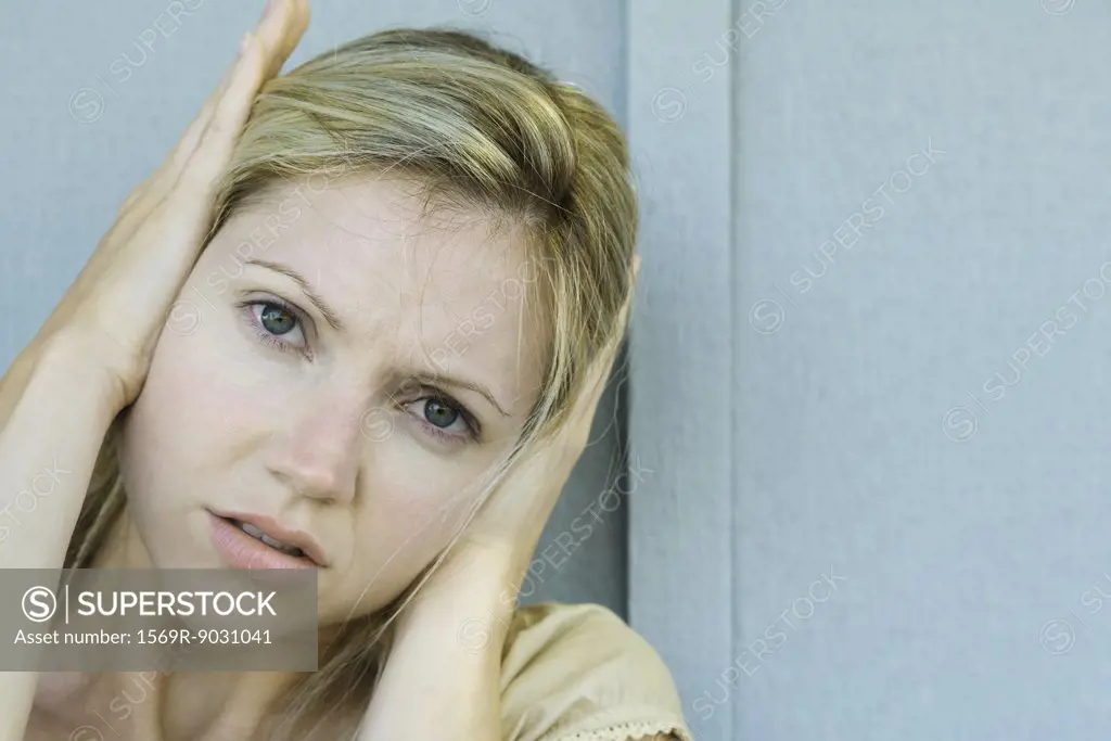 Woman covering ears with hands, frowning at camera