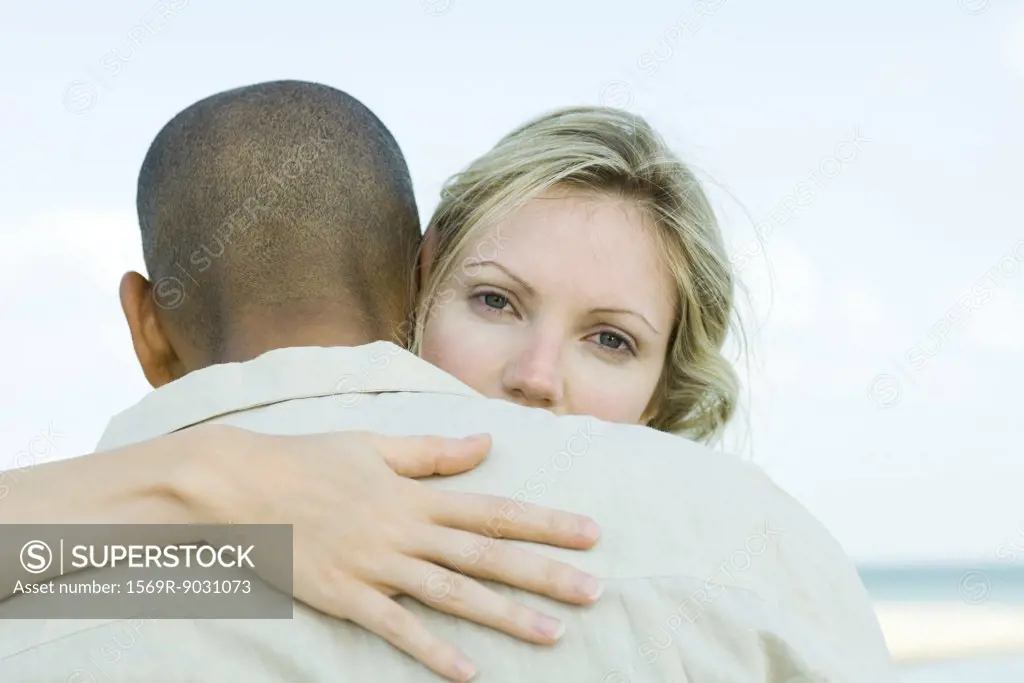 Woman embracing man, looking over his shoulder at camera