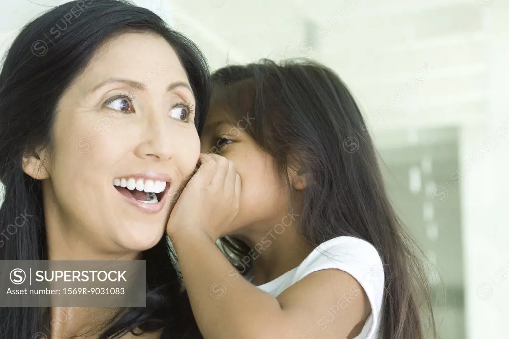 Girl whispering in mother's ear, close-up