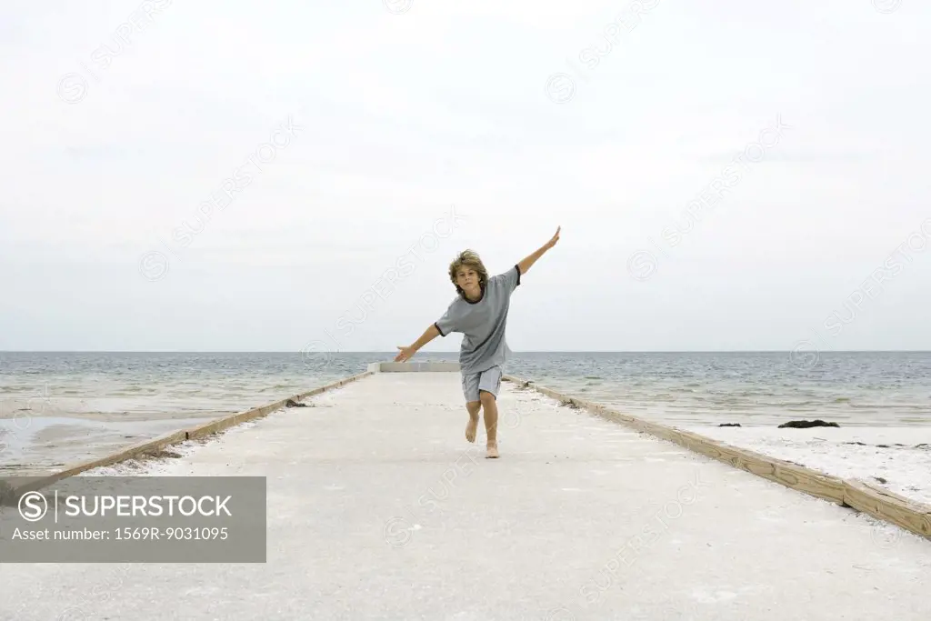 Boy running at the beach with arms outstretched, front view