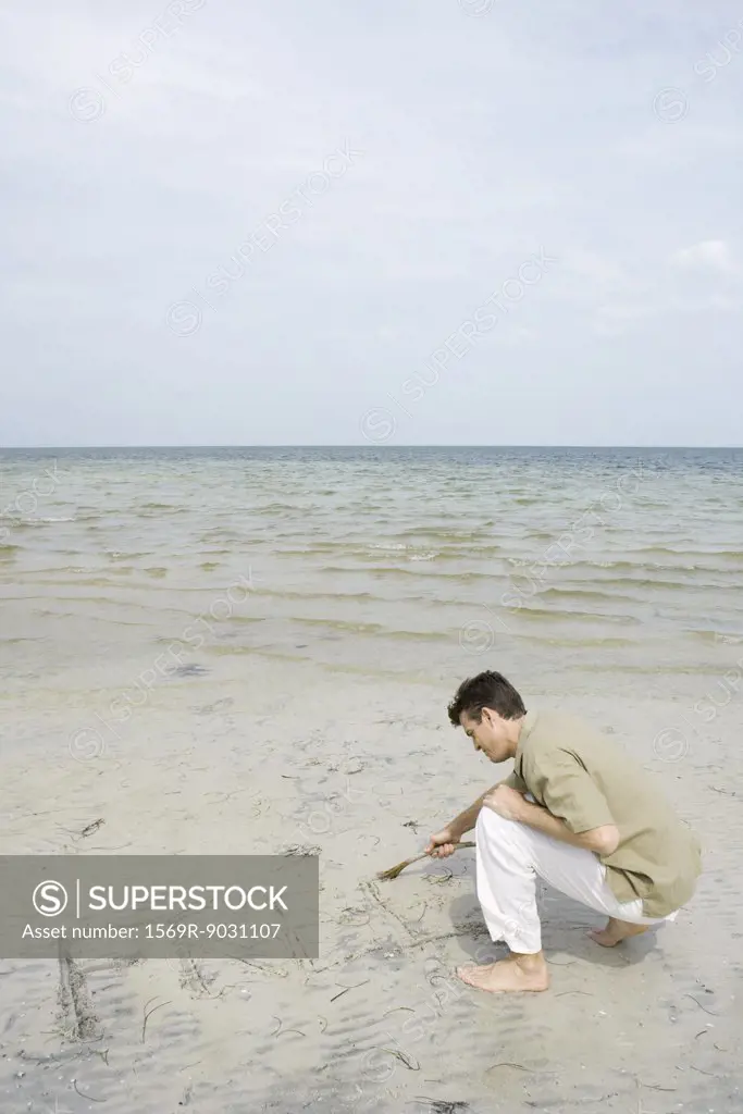 Man crouching on beach writing the word 'free' in sand with a stick
