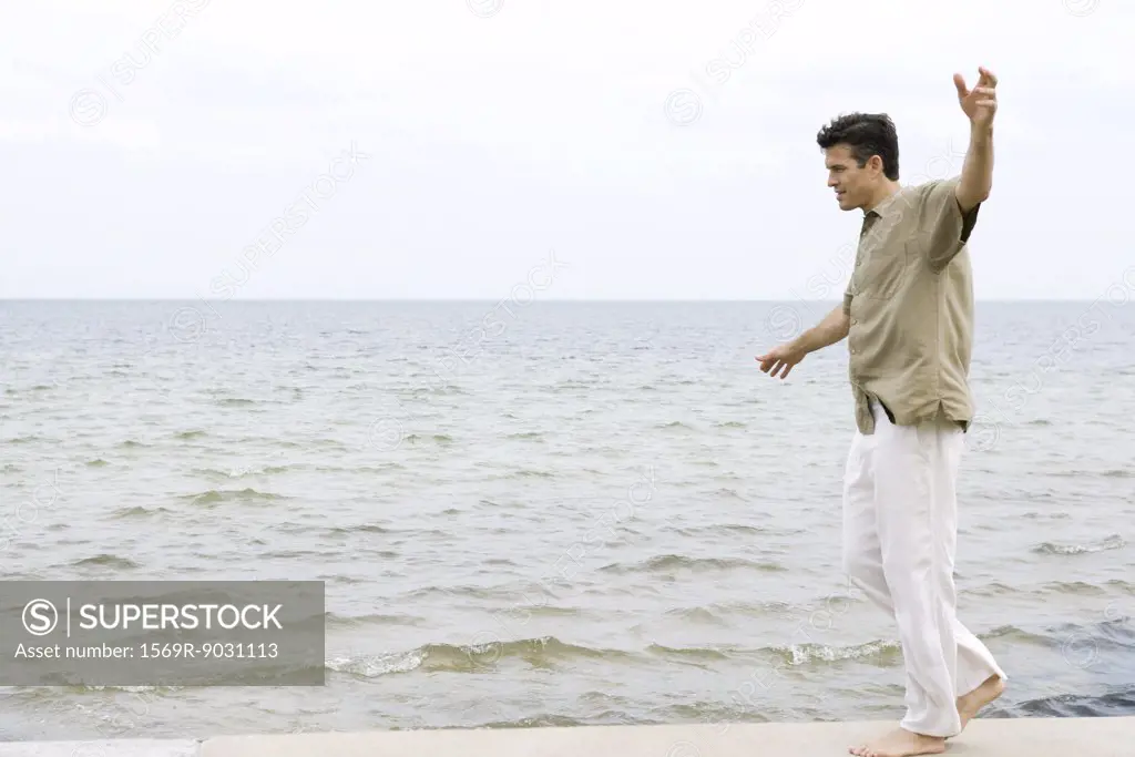 Man walking barefoot with arms out along water's edge