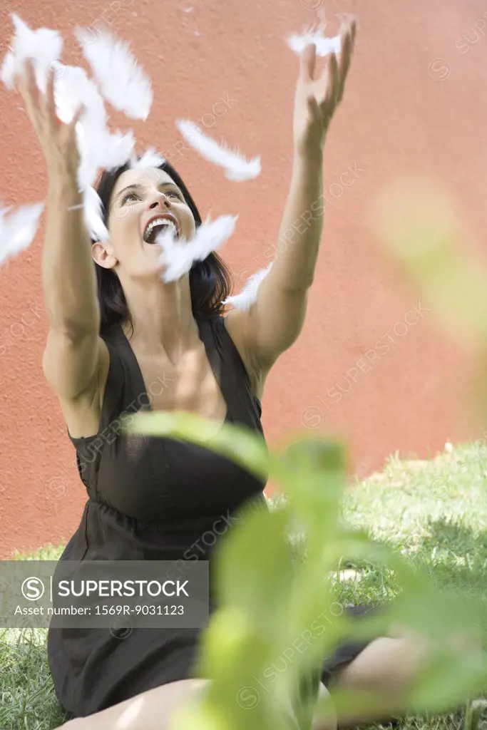 Woman sitting on the ground with arms raised to catch feathers, smiling