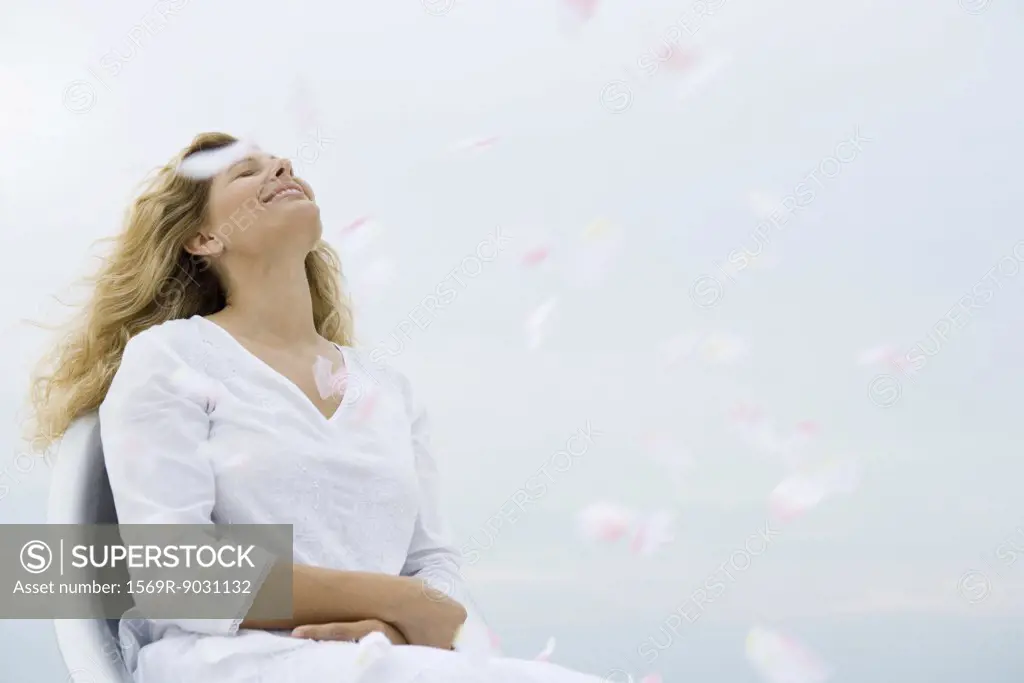 Woman sitting with head back and eyes closed among floating flower petals