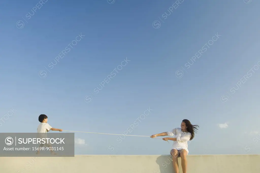 Boy and woman playing tug of war, blue sky in background
