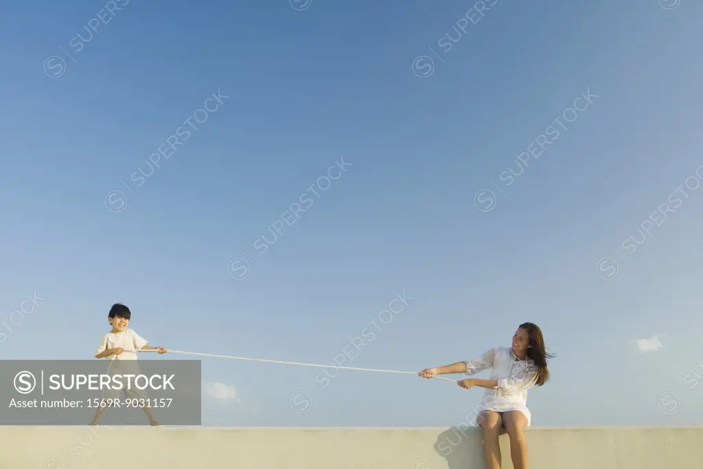 Little boy and woman playing tug of war, blue sky in background