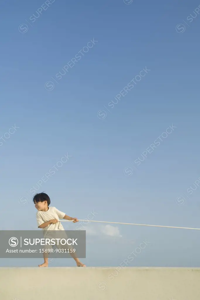 Little boy pulling on rope, blue sky in background, full length