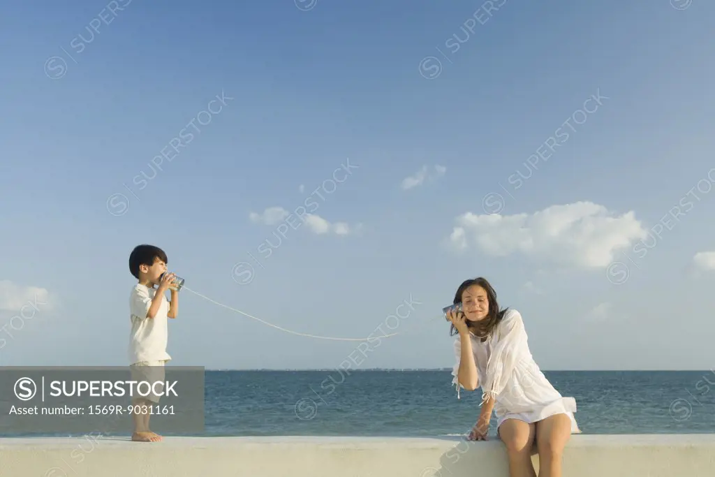 Boy speaking to woman through tin can phone, ocean horizon in background