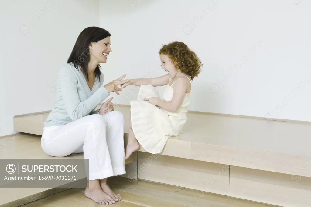 Mother and little girl playing rock paper scissors, laughing, full length